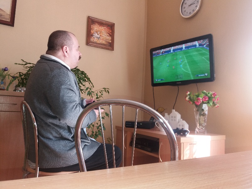 Mężczyznę siedzi na krześle przed telewizorem wiszącym na ścianie.