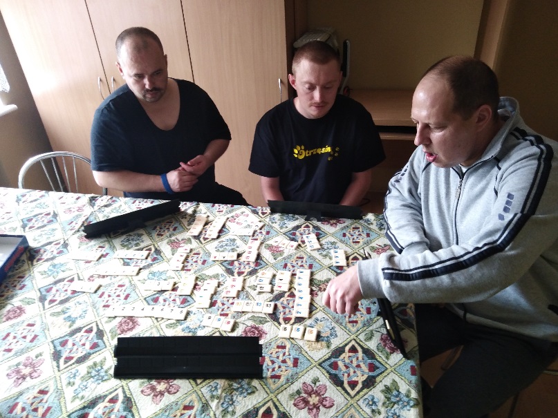 Trzech mężczyzn  przy stolę grających w grę stolikową. 