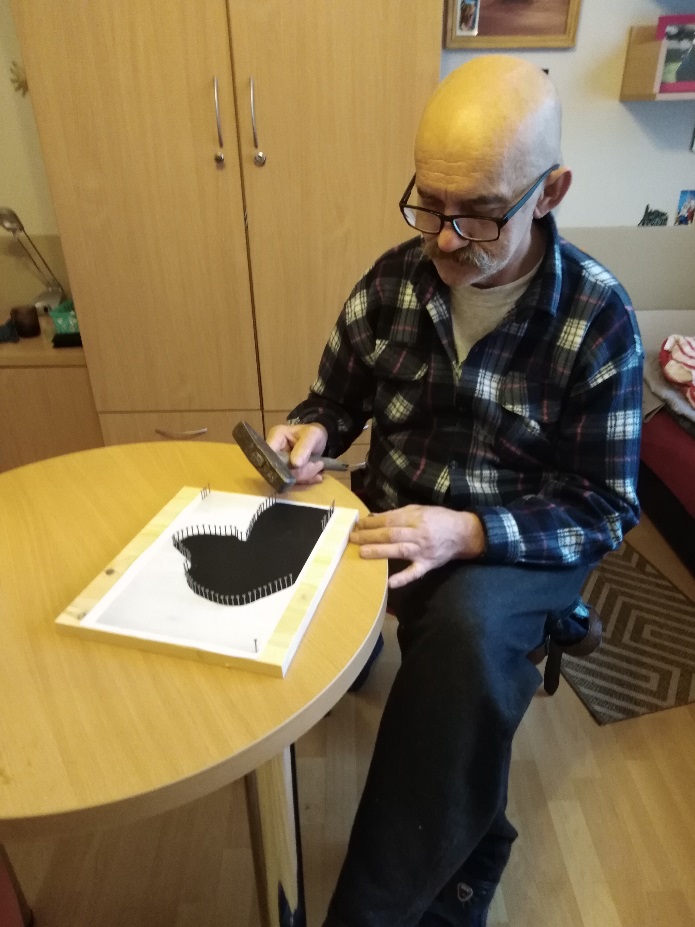 Mężczyzna z młotkiem w ręku przybija gwoździki do drewnianej deski.