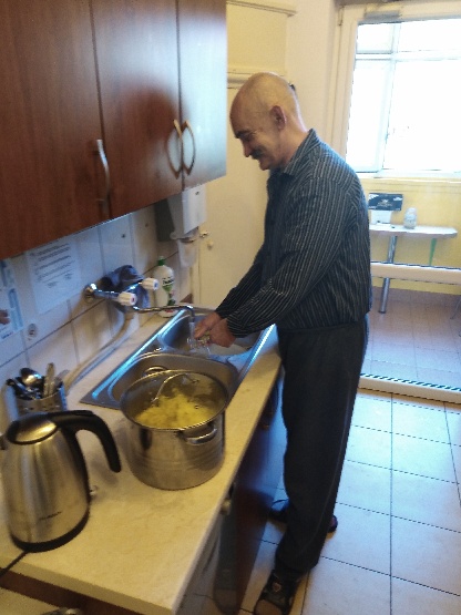  Mężczyzna stojący przy zlewie oraz garnek z obranymi ziemniakami.