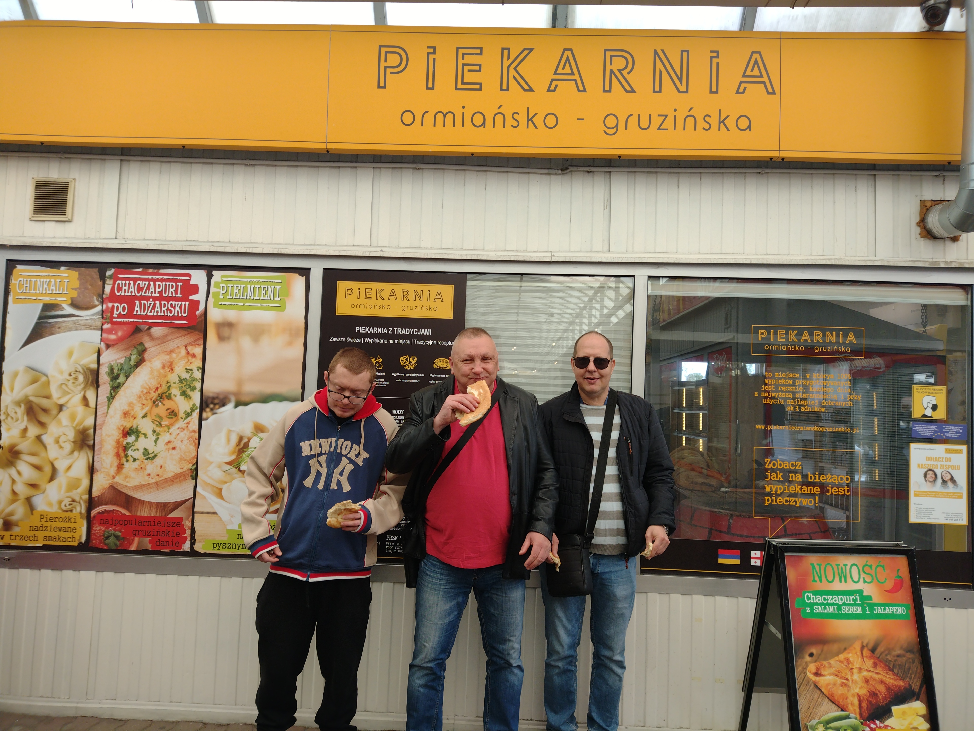 Trzech mężczyzn stoi przed piekarnią.