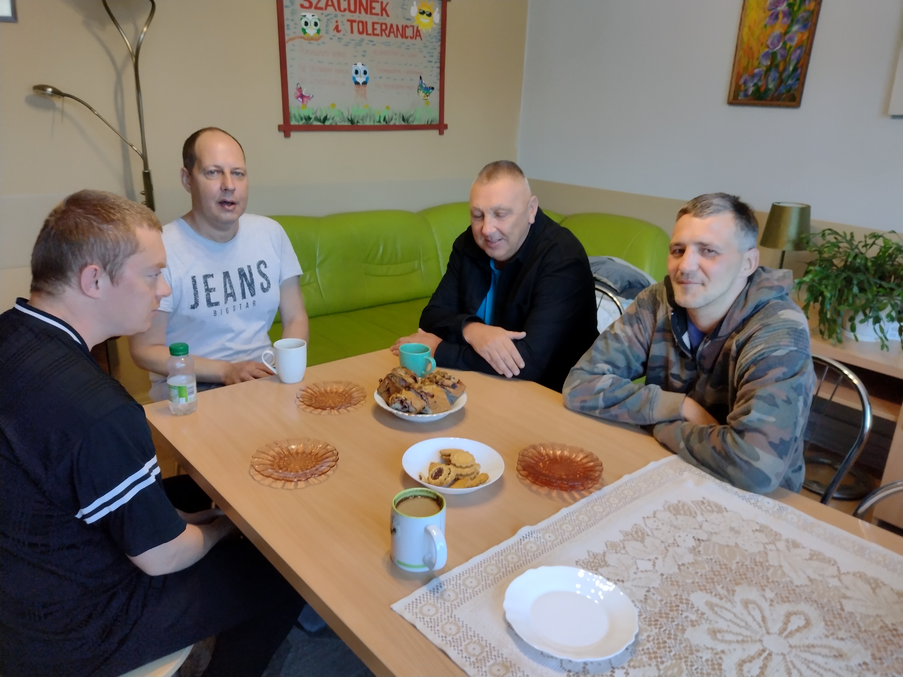 Mężczyźni siedzą przy stole z kawą i słodkościami.