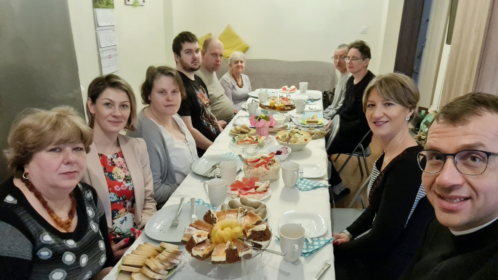 Grupa Kobiet imężczyzn siedząca przy stole z potrawami wielkanocnymi.
