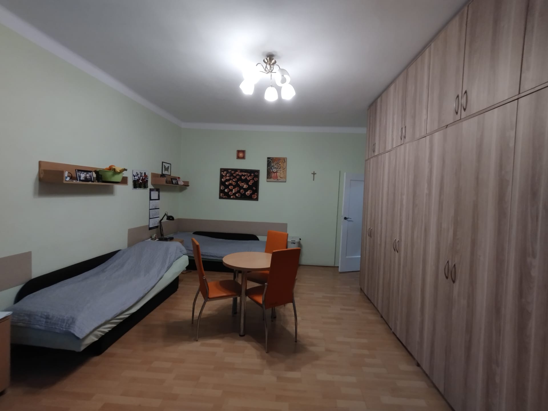 Pokój z dwoma pojedyńczymi łóżkami oraz okrągłym stołem i dwoma pomarańczowymi krzesłami.