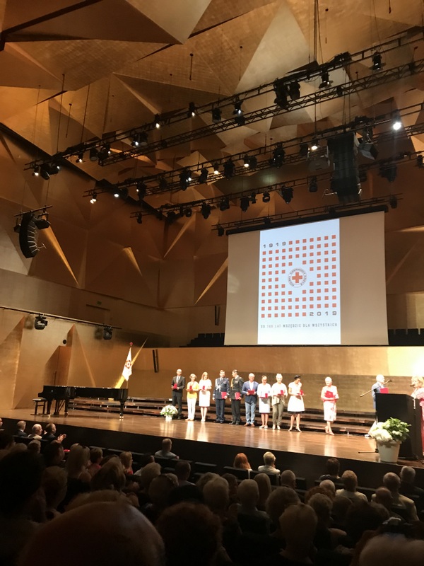 Sala widowiskowa w Filharmonii, na scenie wyróżnione osoby, plakat PCK, publiczność