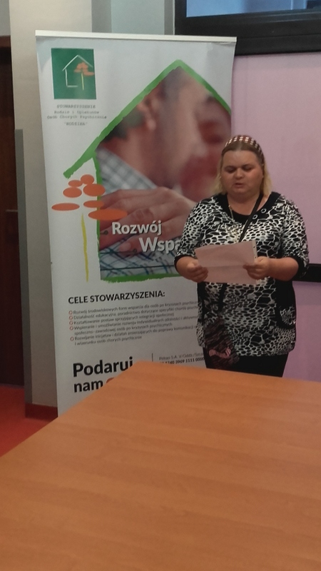 Kobieta czytająca z kartki utwór, baner Stowarzyszenia Rodzin i Opiekunów Osób Chorujących Psychicznie „Rodzina” 