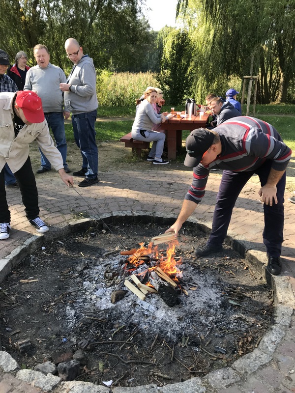 Palenisko do  grillowania w parku przy którym uczestnicy piekają kiełbaski, miejsca siedzące  do konsumpcji.