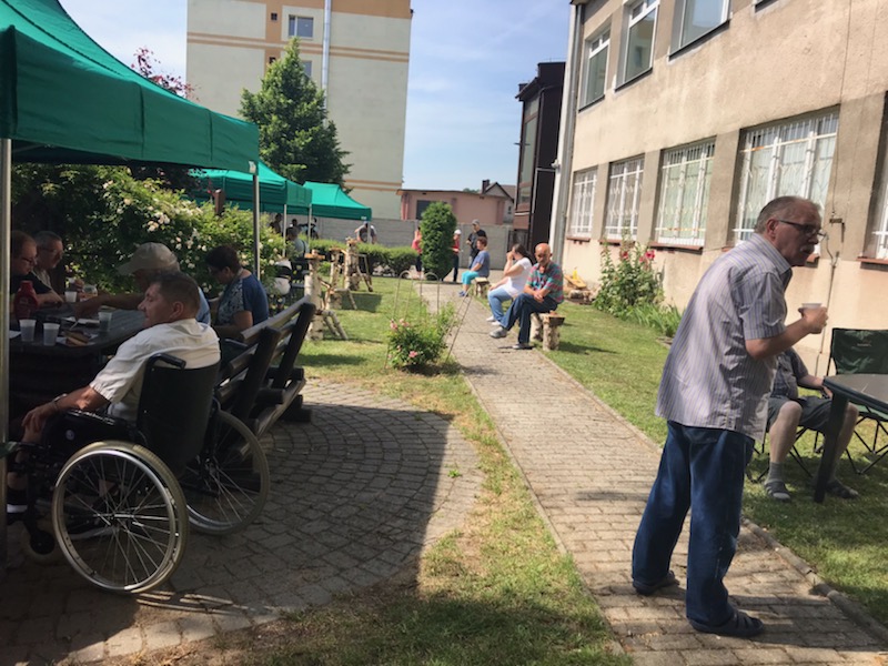 Trzy namioty turystyczne dające cień zaproszonym gościom, kobiety i mężczyźni grillujący w ogrodzie