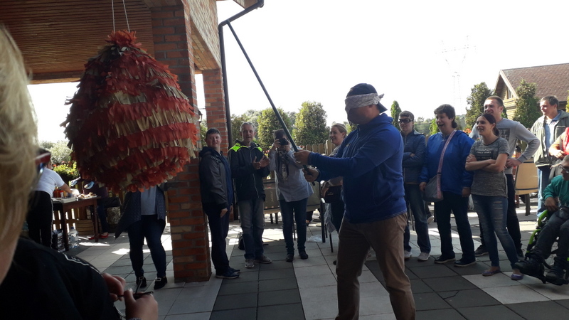 Grupa uczestników otaczających wokół mężczyznę rozbijającego piniatę – ozdobny worek z cukierkami