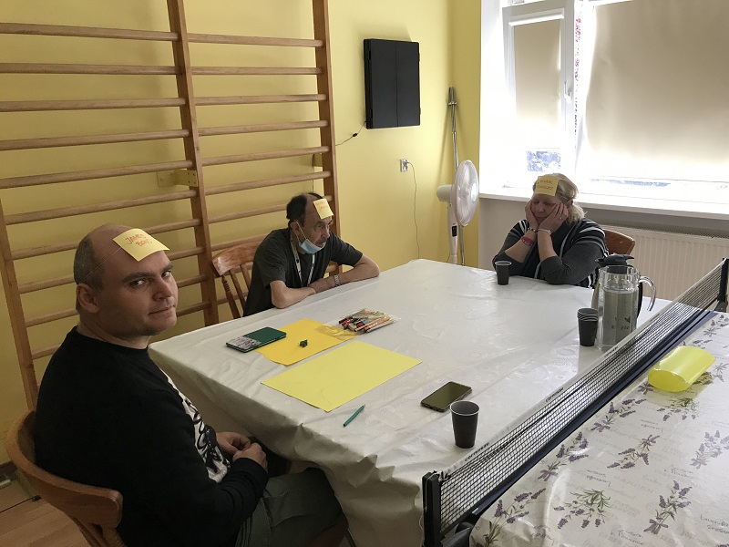 Dwóch mężczyzn i kobieta siedzących przy stole na zajęciach z ludoterapii