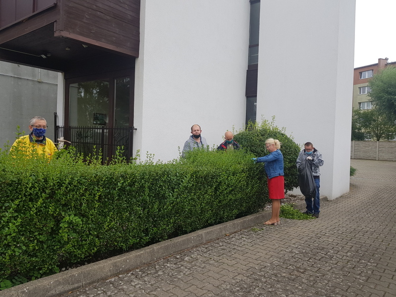 Czterech mężczyzn i terapeuta strzygą żywopłot przed naszym domem.