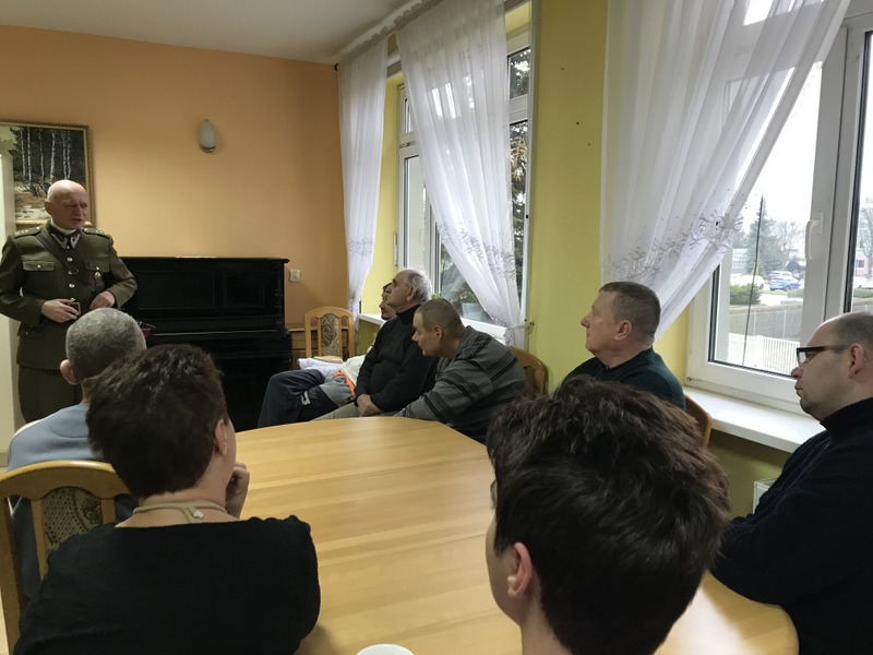 Grupa uczestników przebywających w świetlicy słucha wykładu żołnierza. 