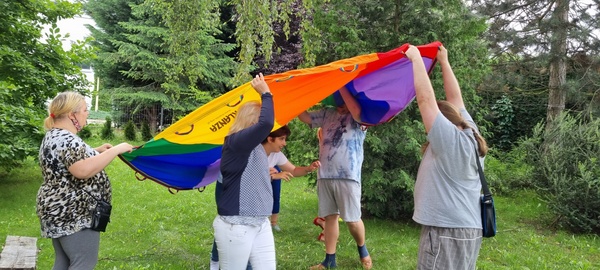 Trzy kobiety i dwóch mężczyzn trzymających chustę Klanza w ogrodzie.