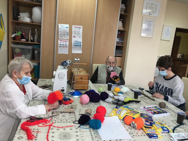 Dwaj mężczyźni siedzą w pracowni plastycznej i wykonują prace manualne.