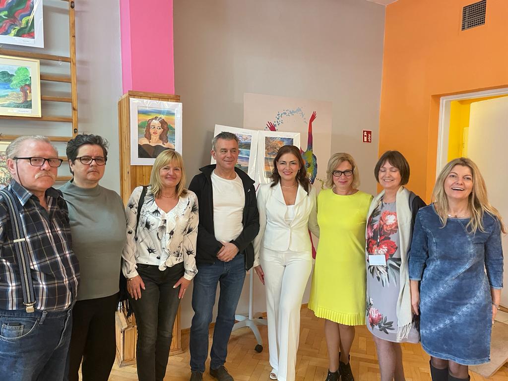 Grupa kobiet i mężczyzn pozuje do zdjęcia  na tle obrazów.  