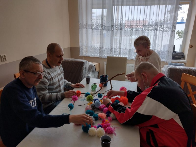 Trzech mężczyzn i kobieta wieszają pompony z wełny na gałązkach.