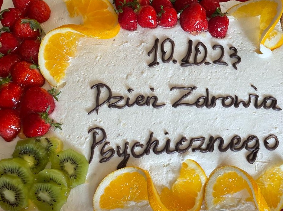 Tort z napisem „10.10.23 Dzień Zdrowia Psychicznego” ozdobiony pomarańczami, truskawkami i kiwi.