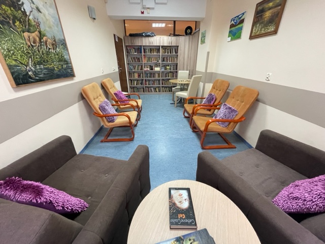 Miejsce biblioteczne, w którym znajdują się cztery fotele, stolik oraz regał z książkami