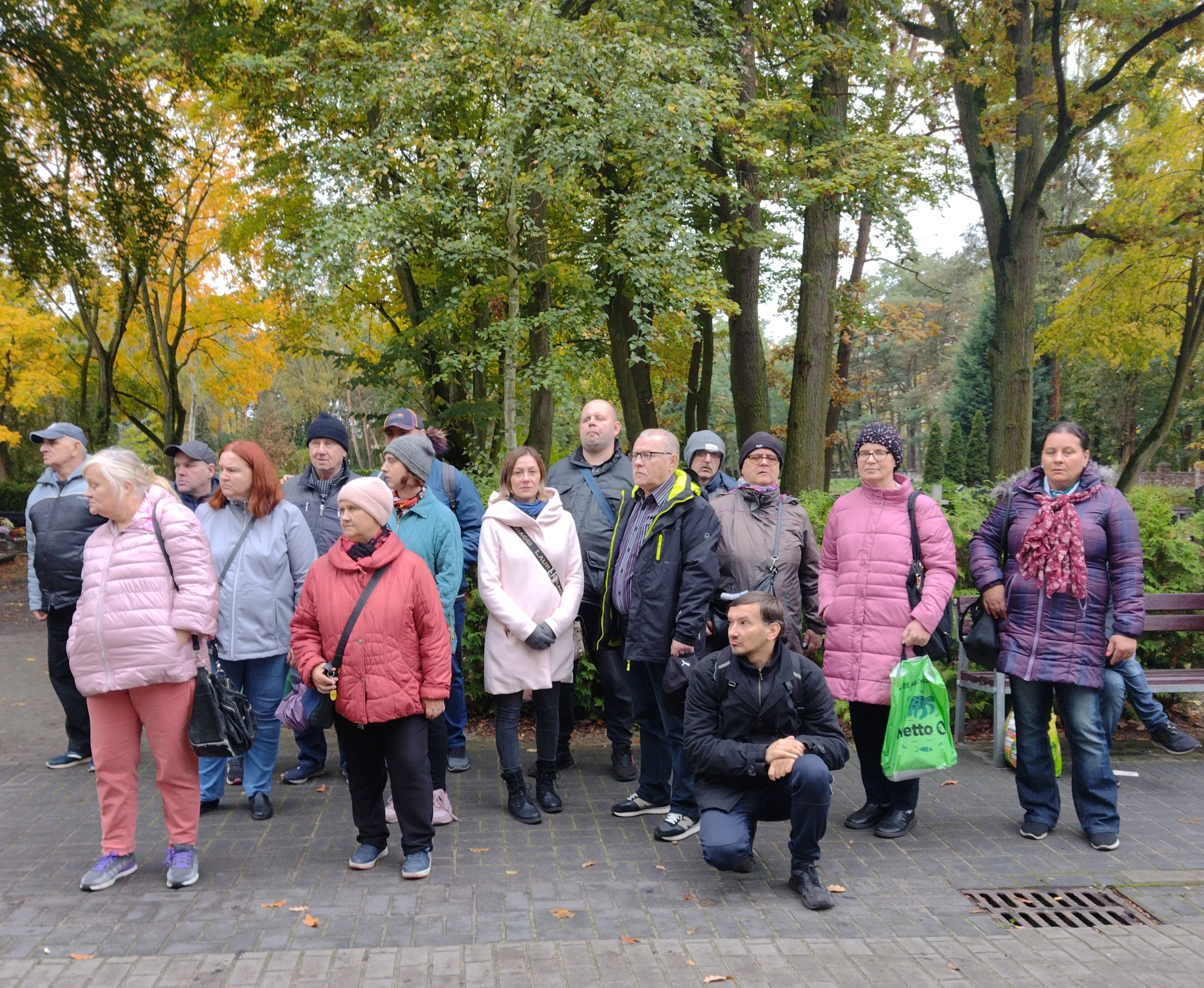 Grupa kobiet i mężczyzn stoją pozując do zdjęcia. W tle drzewa z zielonożółtymi liśćmi.