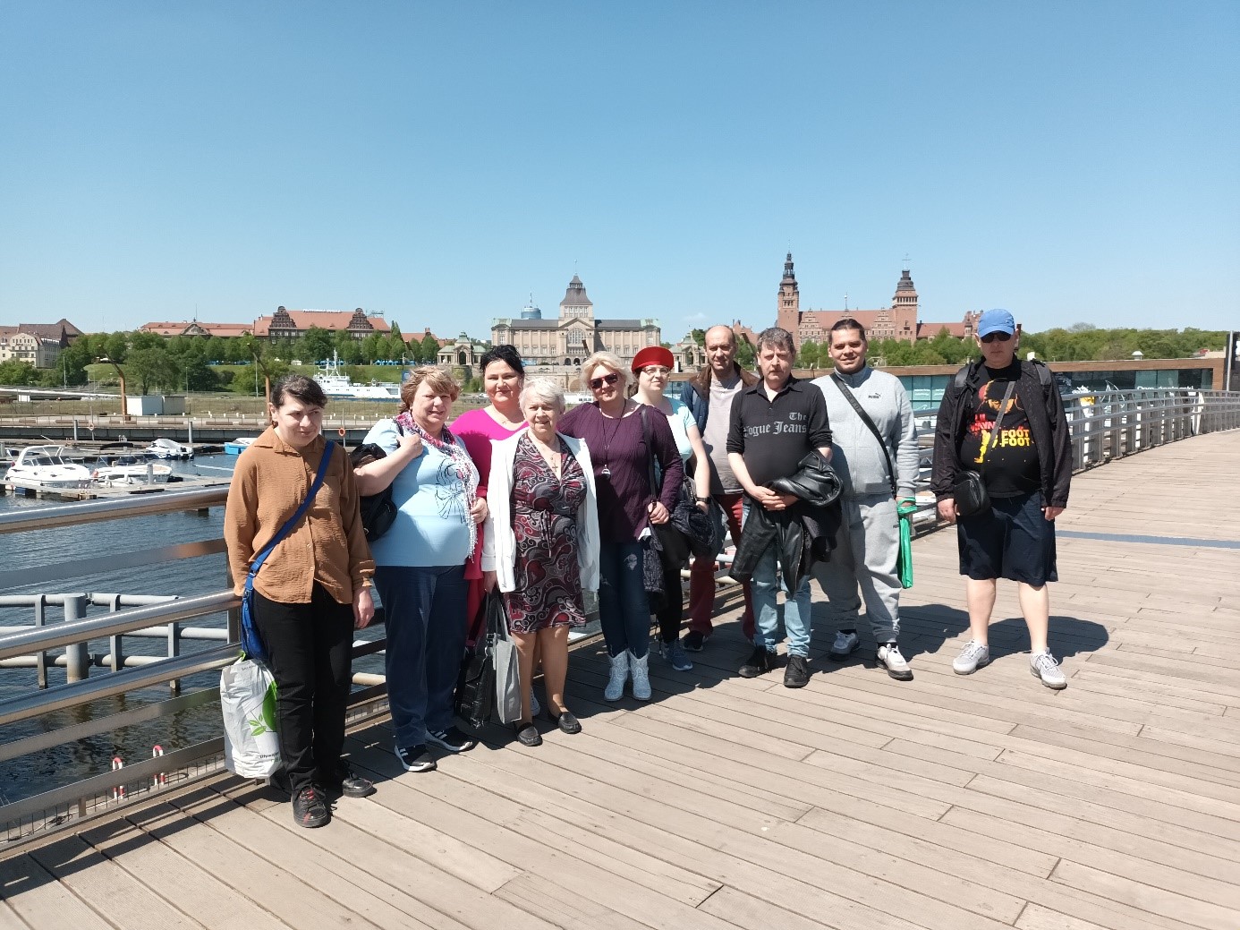 Grupa osób pozująca do zdjęcia na moście. W tle panorama miasta. 