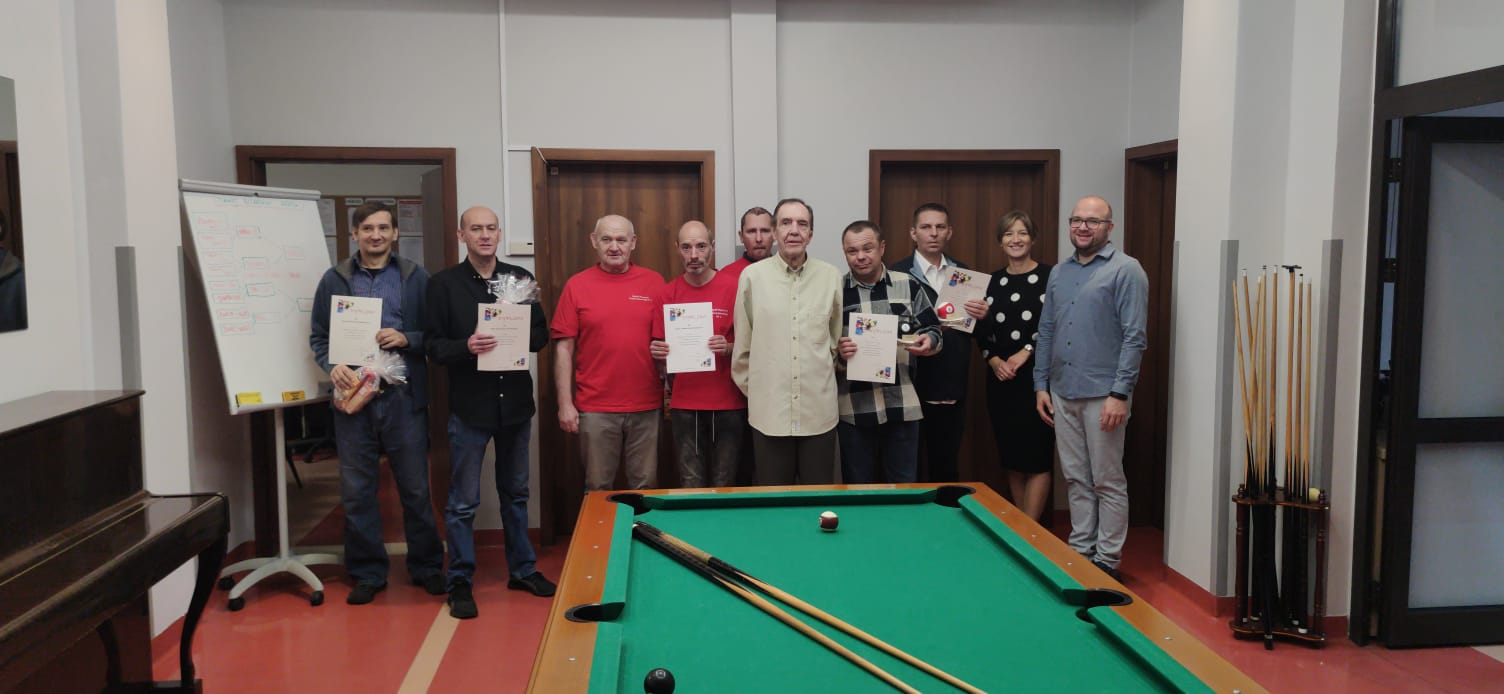 : Na pierwszym planie zielony stół do bilardu z leżącymi kijami,  za nim 10 osób stoi z dyplomami w rękach pozując do zdjęcia.
