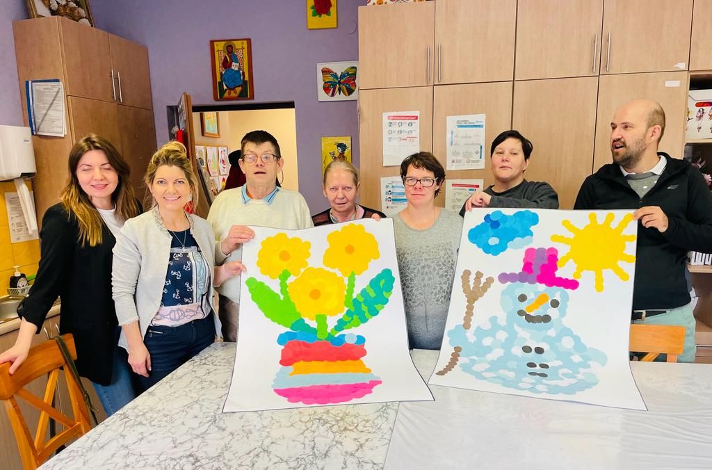 Grupa osób stoi z pracami plastycznymi 