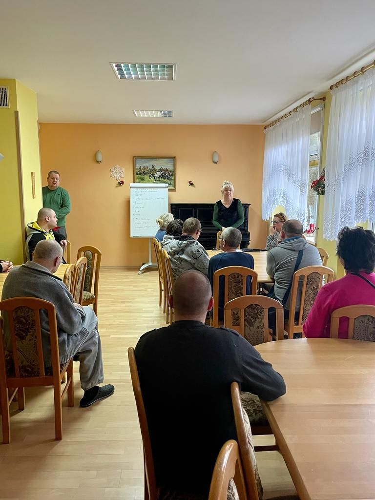 Grupa kobiet i mężczyzn słucha wykładu terapeuty.  
