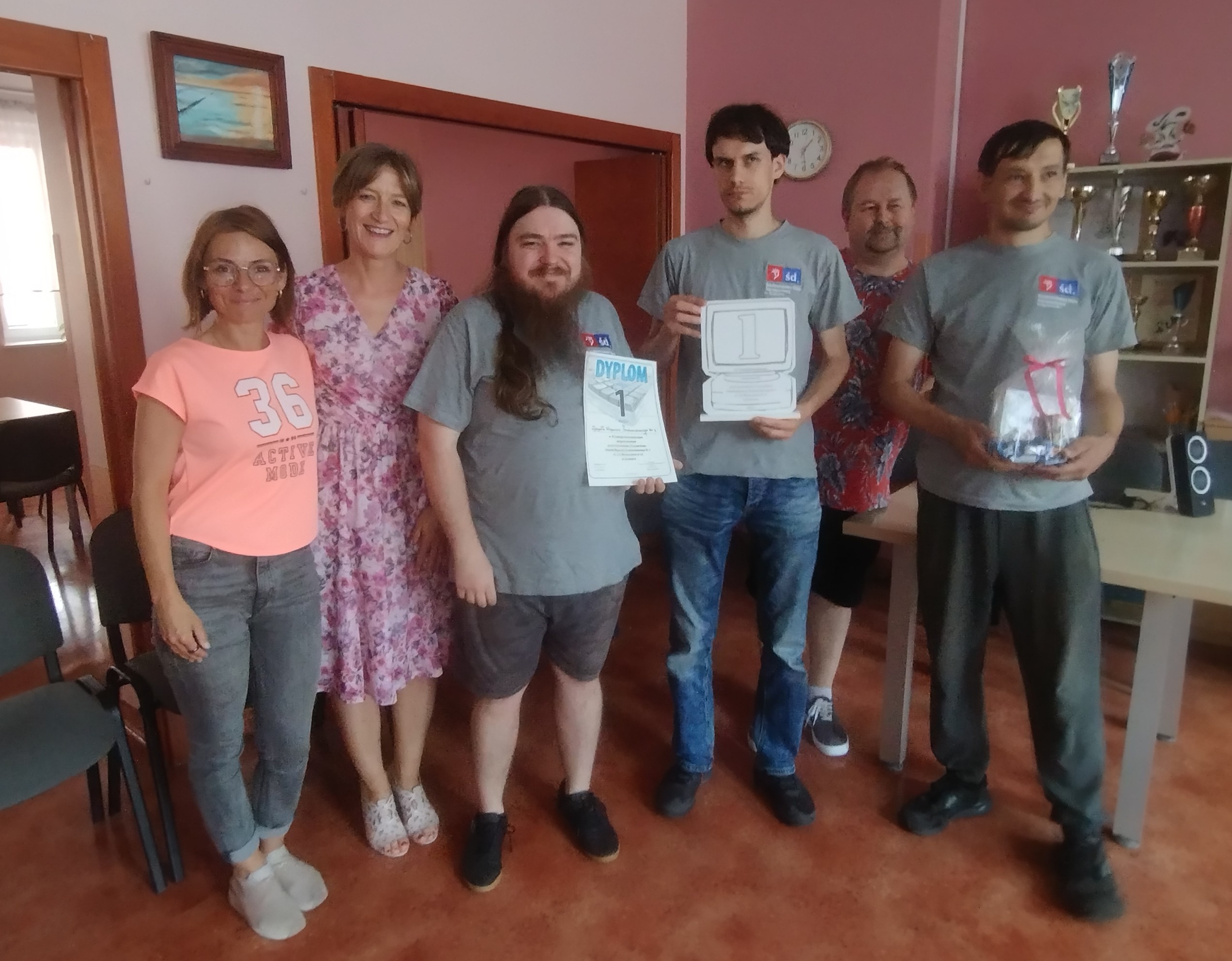 2 kobiety i 4 mężczyzn stoją pozując do zdjęcia, trzymają dyplom, trofeum i słodką nagrodę.
