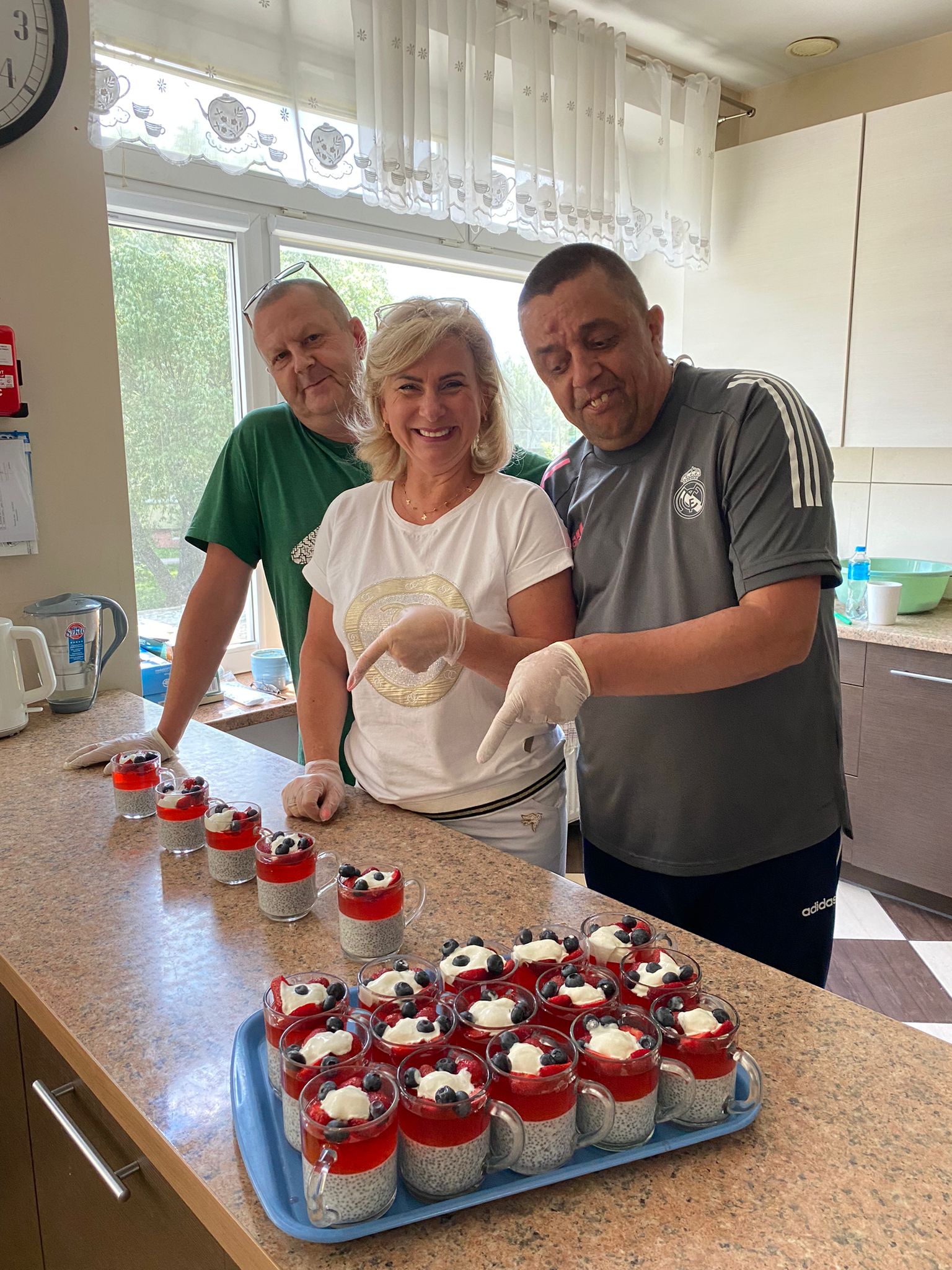 Kobieta i dwóch mężczyzn prezentują na blacie kuchennym własnoręcznie przygotowane desery. 