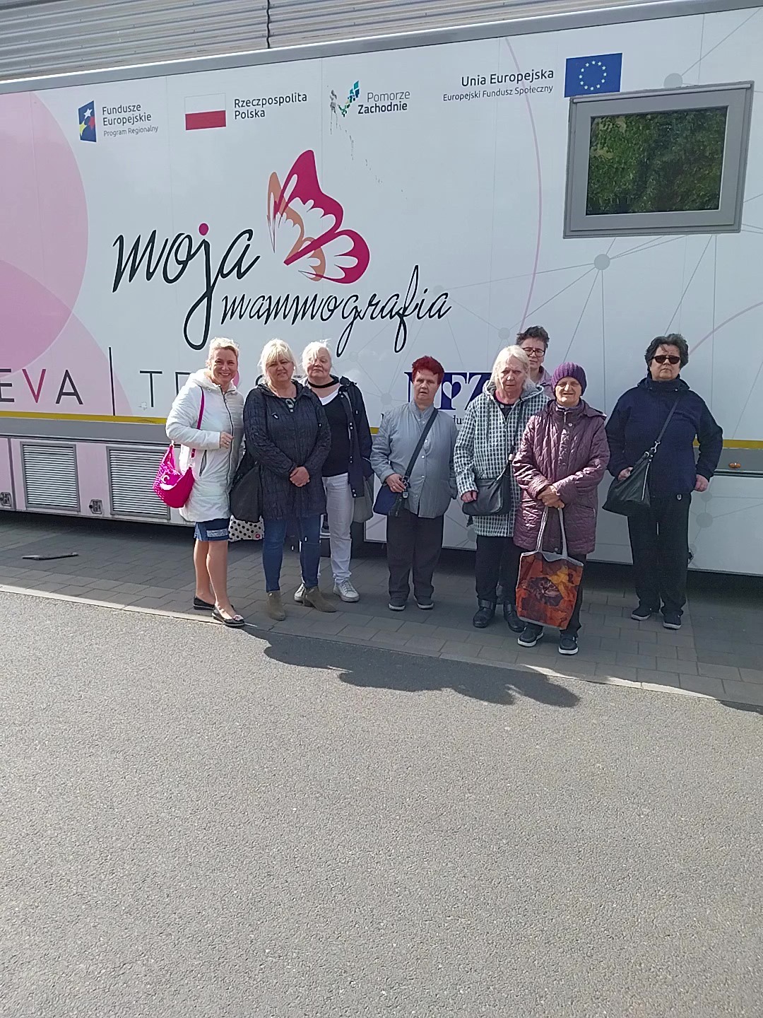 Grupa ośmiu kobiet stoi przed mammobusem i pozuje do zdjęcia. 