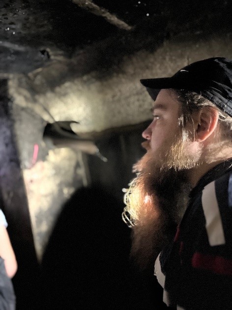 W ciemnych, piwnicznych pomieszczeniach stoi mężczyzna z brodą. W tle lecący nietoperz. 