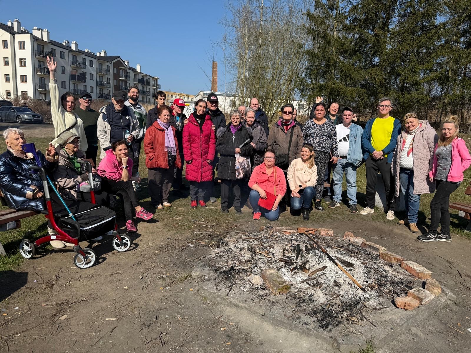Grupa kobiet i mężczyzn pozuje do zdjęcia przy dogasającym ognisku. 