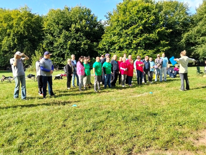 W słoneczny dzień, na zielonej trawie stoi grupa osób w kolorowych koszulkach.