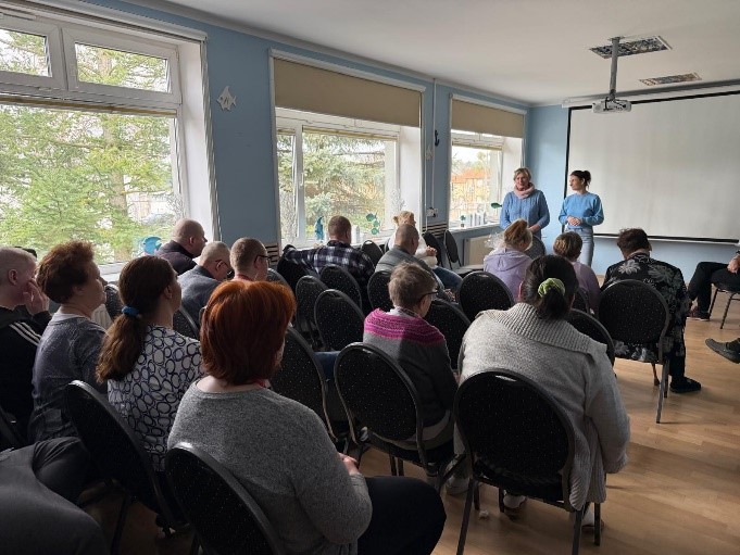 Grupa kobiet i mężczyzn siedzą na krzesłach podczas wykładu. 