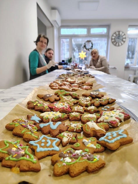Na zdjęciu widać długi stół przykryty papierem do pieczenia, na którym ułożone są kolorowo udekorowane pierniki w kształcie choinek, gwiazdek i innych świątecznych motywów. 