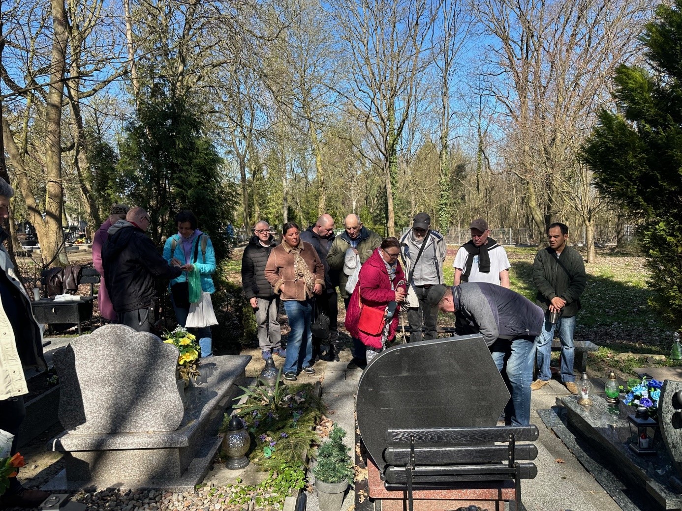 Grupa kobiet i mężczyzn stoją przy grobie.