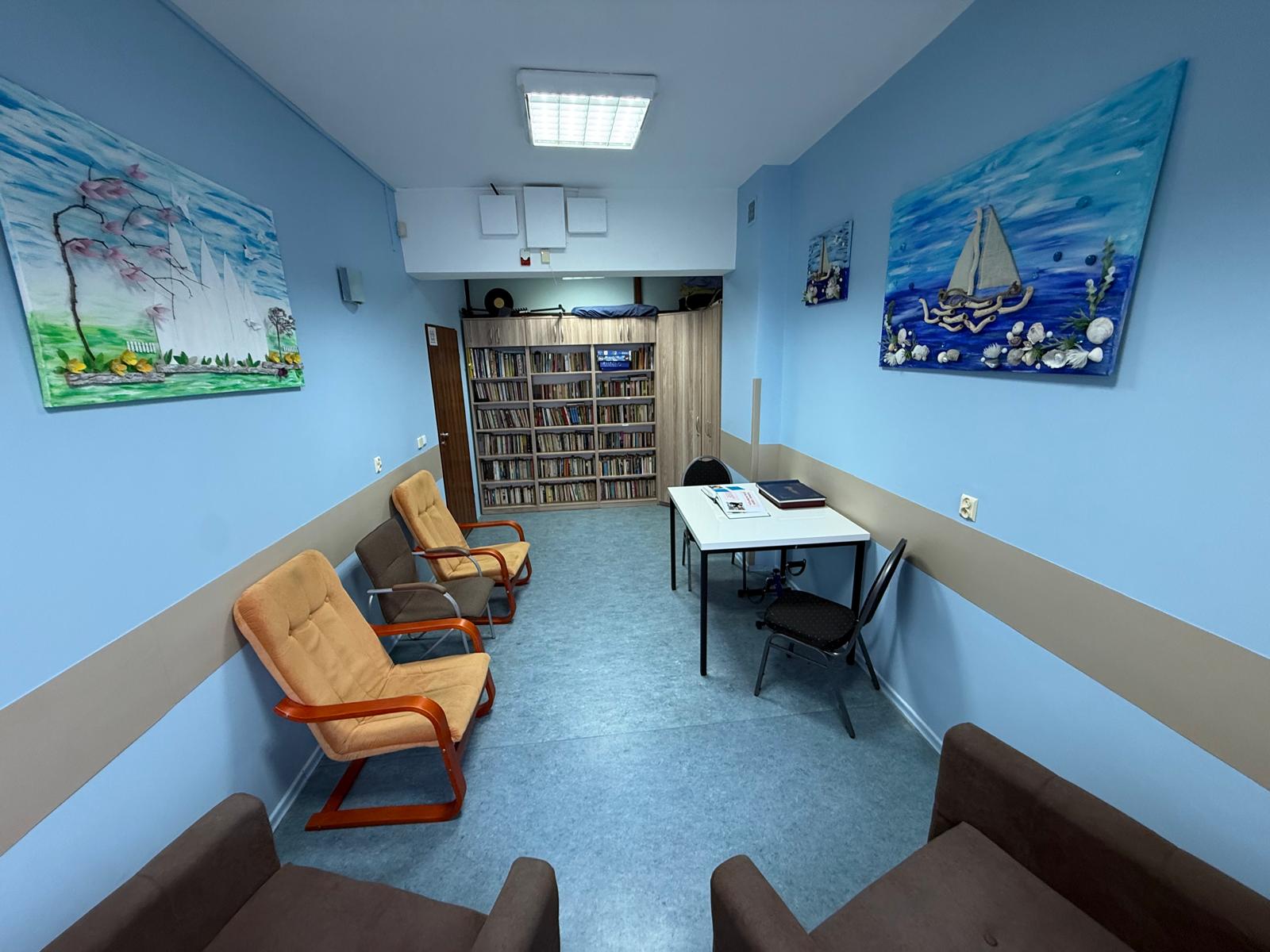 Miejsce biblioteczne, w którym znajdują się cztery fotele, stolik oraz regał z książkami