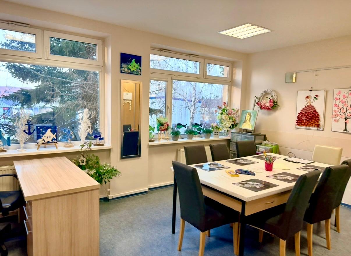 Stół roboczy wraz z dziewięcioma drewnianymi krzesłami oraz stanowisko pracy dla terapeuty . Na regałach znajdują się ozdoby drewniane