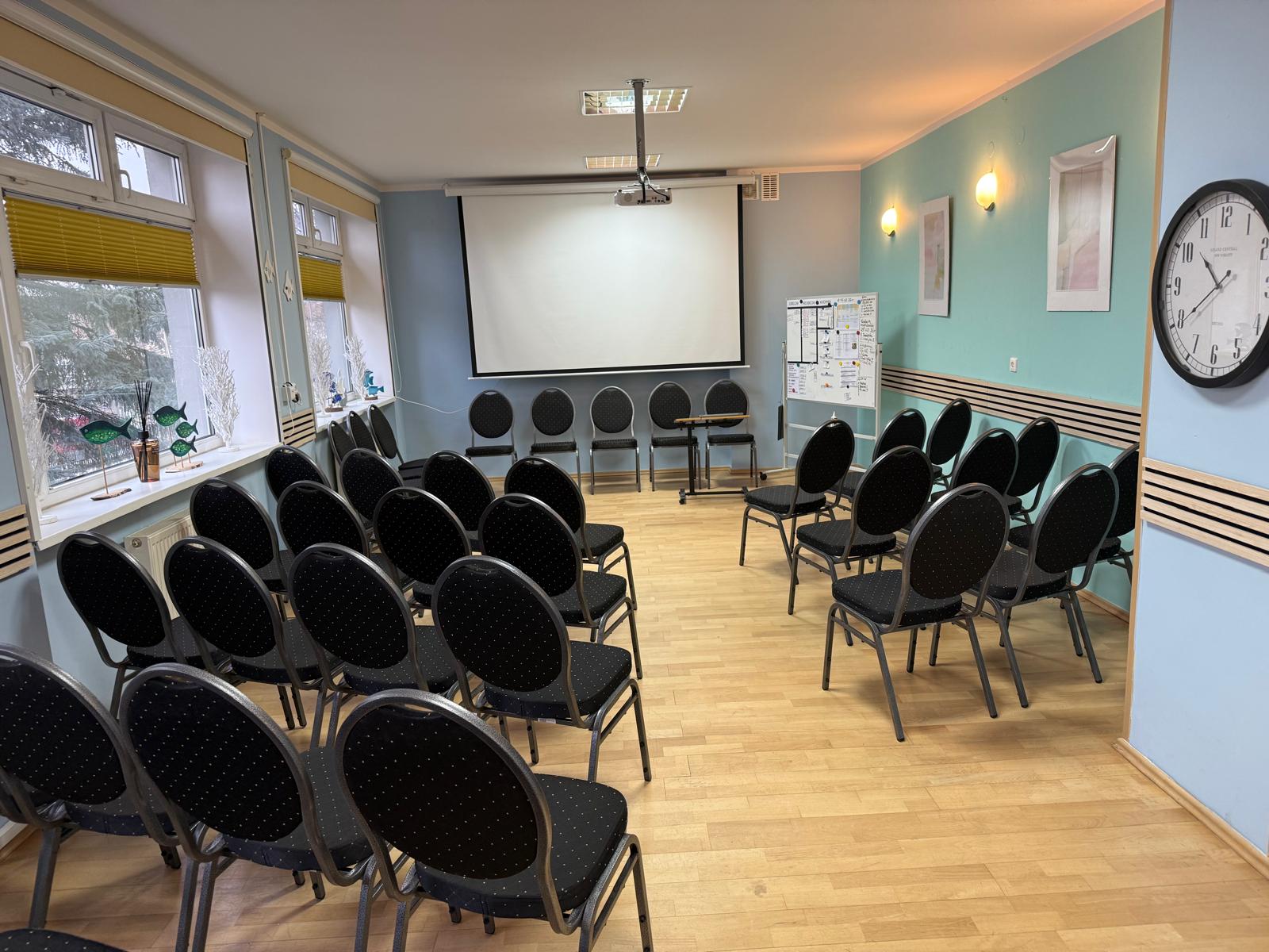 Duża sala z krzesłami oraz sprzętem RTV oraz ekranem.