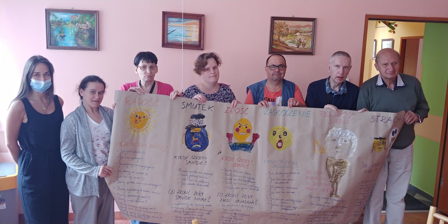 Grupa osób trzyma przed sobą zamalowane farbami arkusze papieru