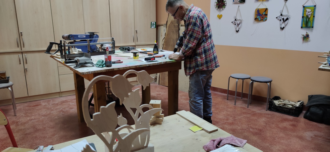 Mężczyzna pochylony przy stole nad kawałkiem drewna.