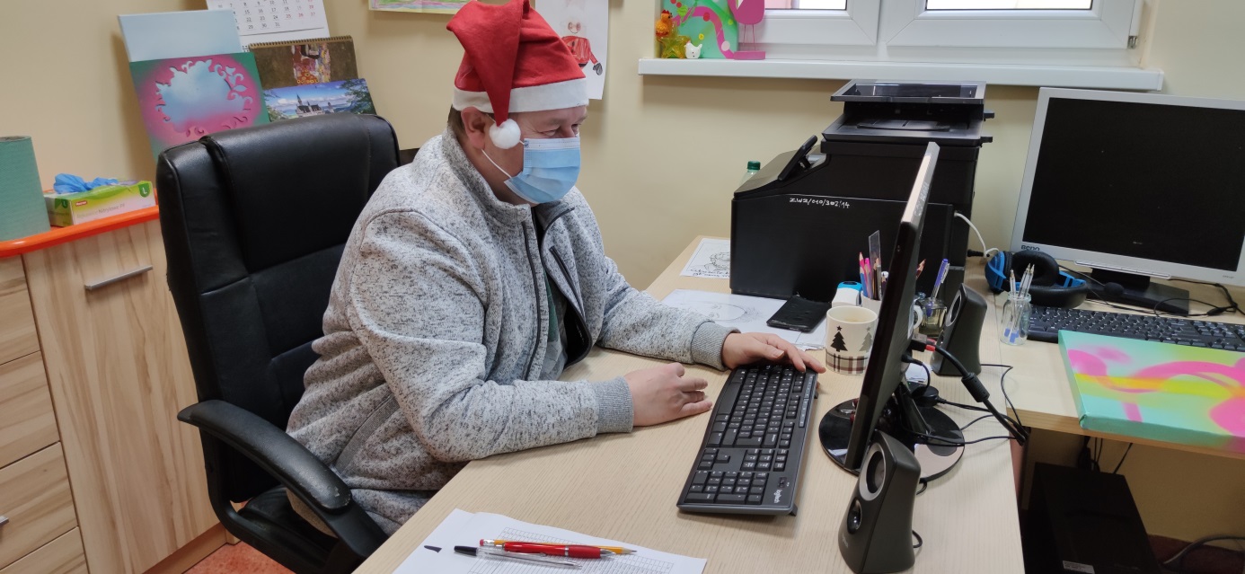 Mężczyzna siedzi przed monitorem w masce i czapce mikołaja.