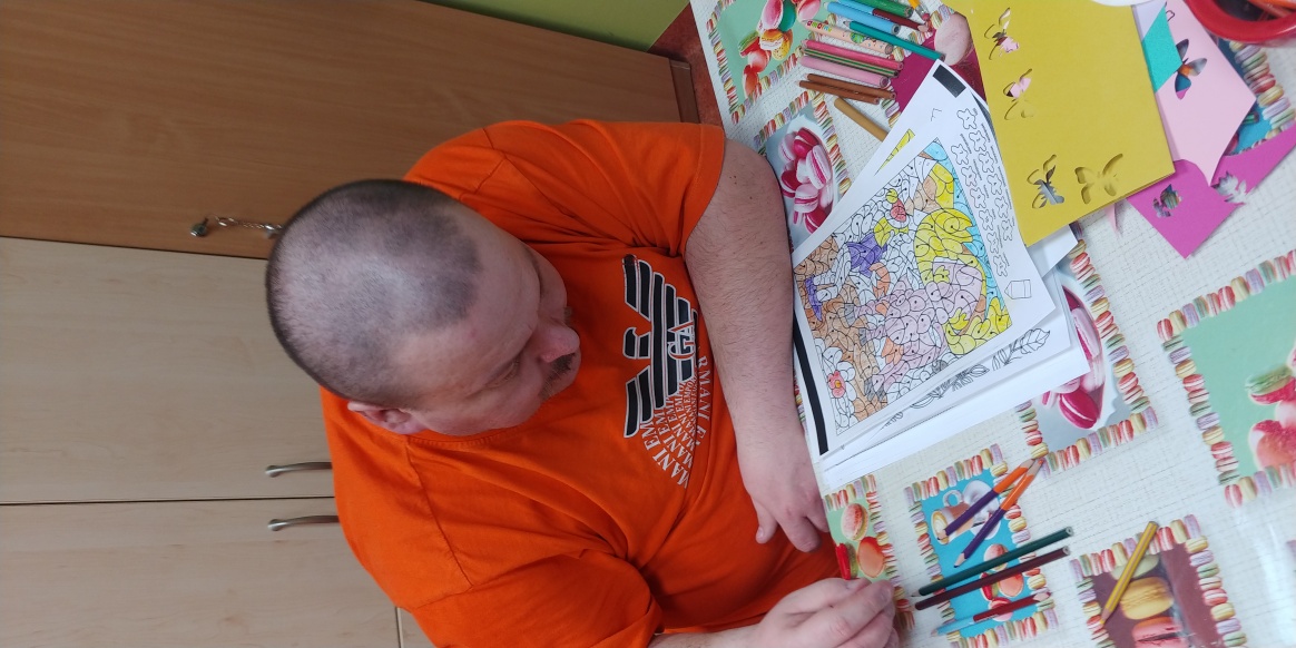 Mężczyzna siedzi przy stole z kolorowankami.