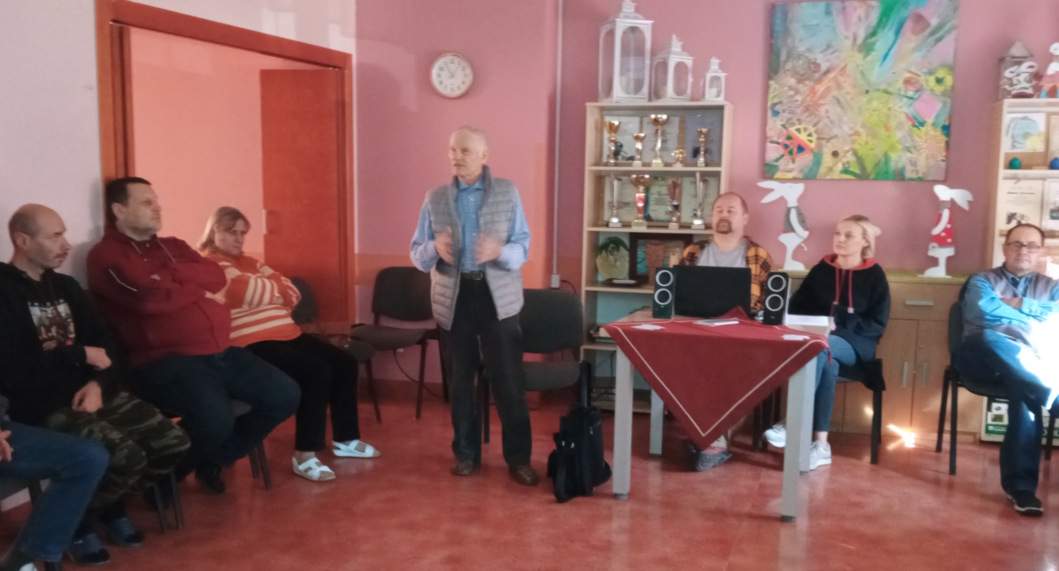 Grupa osób siedzi słuchając prowadzącego.