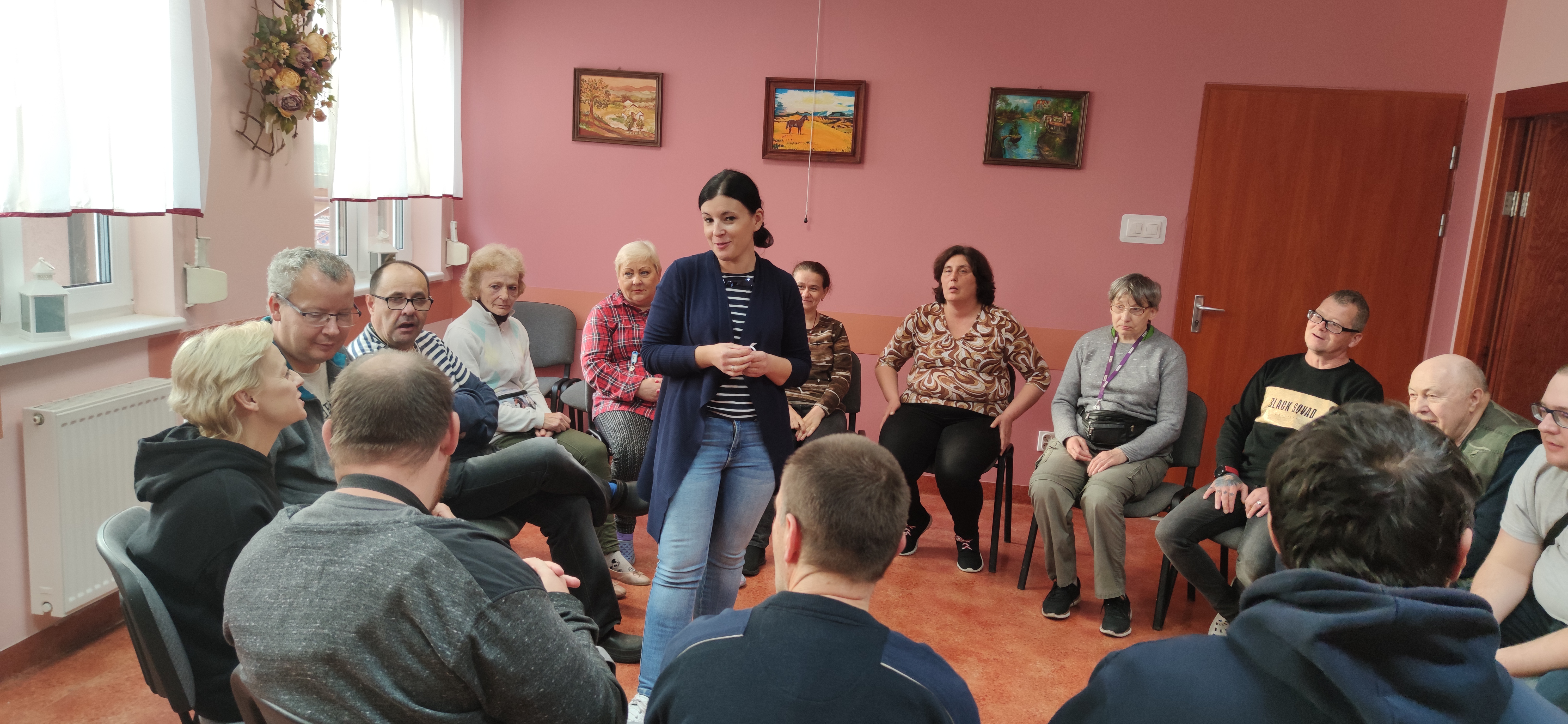 Grupa osób siedzi na krzesłach w kręgu.