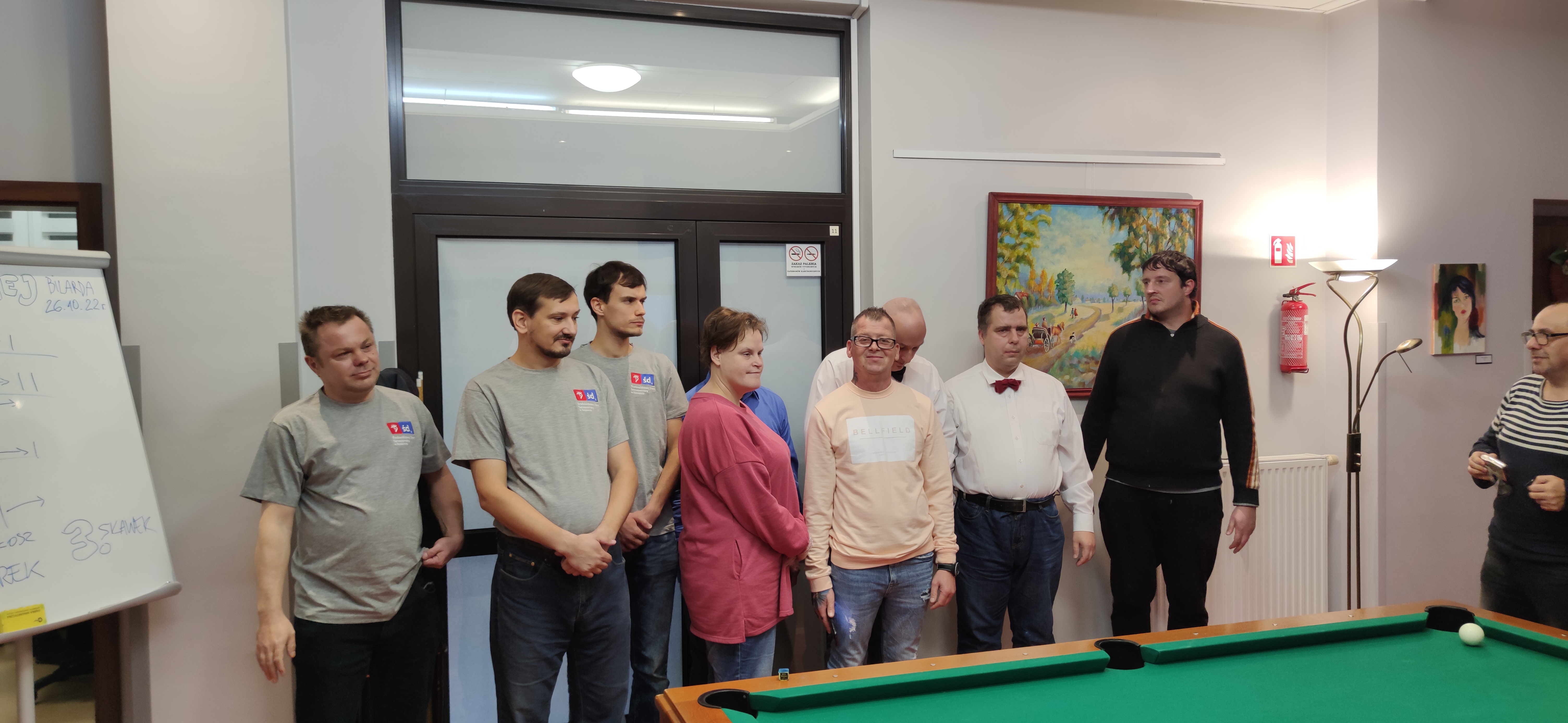 Grupa osób  stoi przy stole bilardowym.