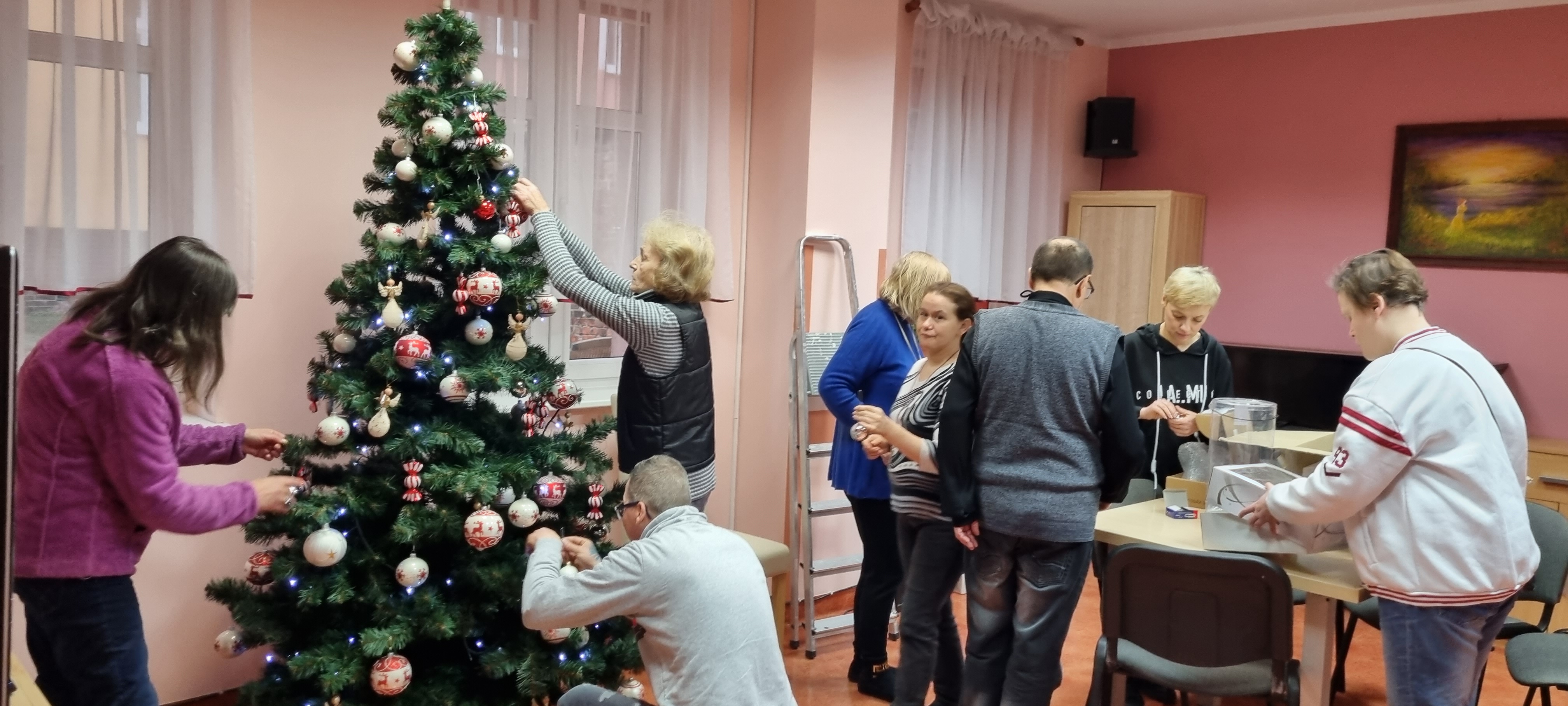 Grupa osób ubiera choinkę.