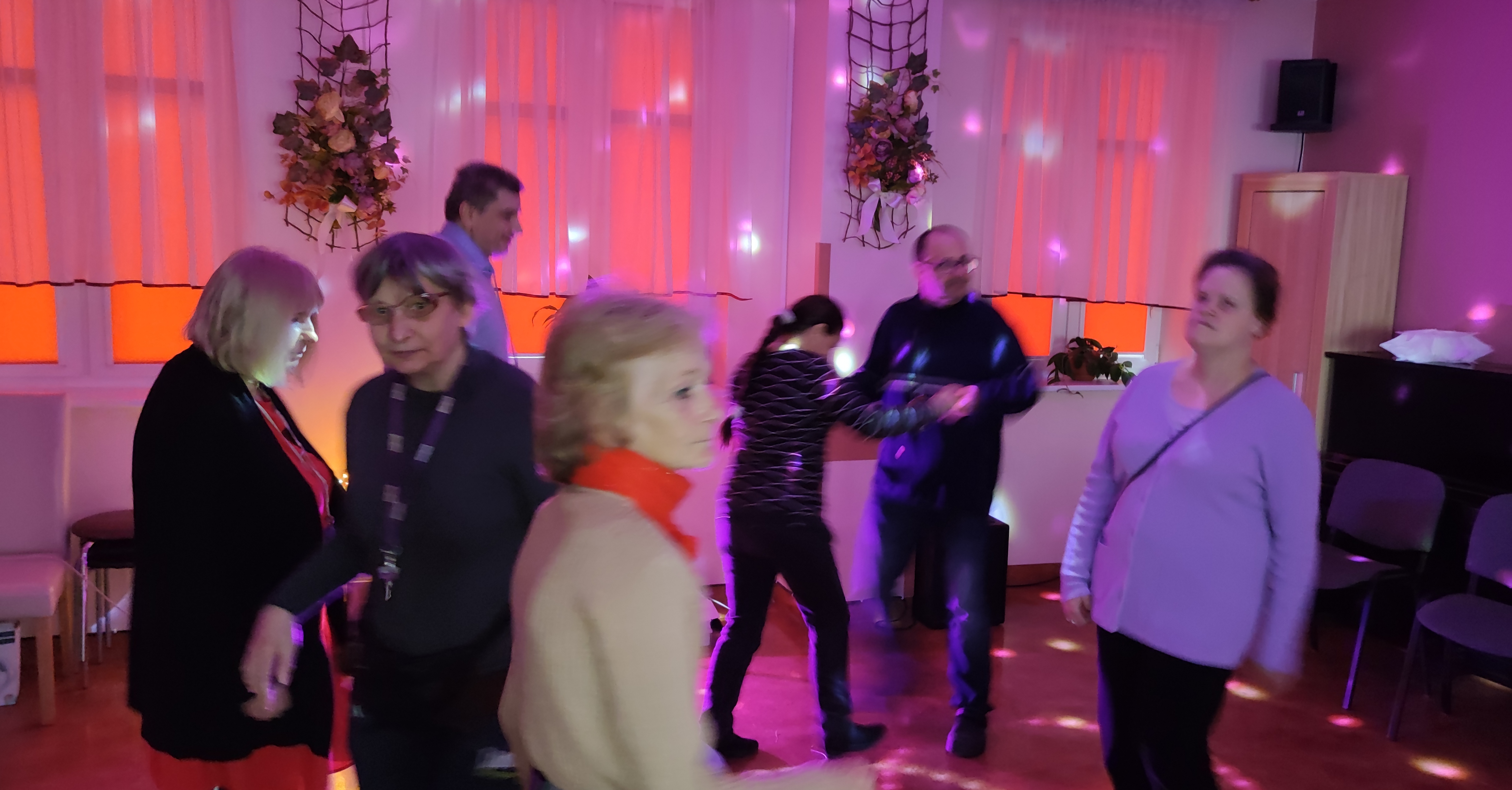 Grupa osób tańczy w sali oświetlonej lampkami.