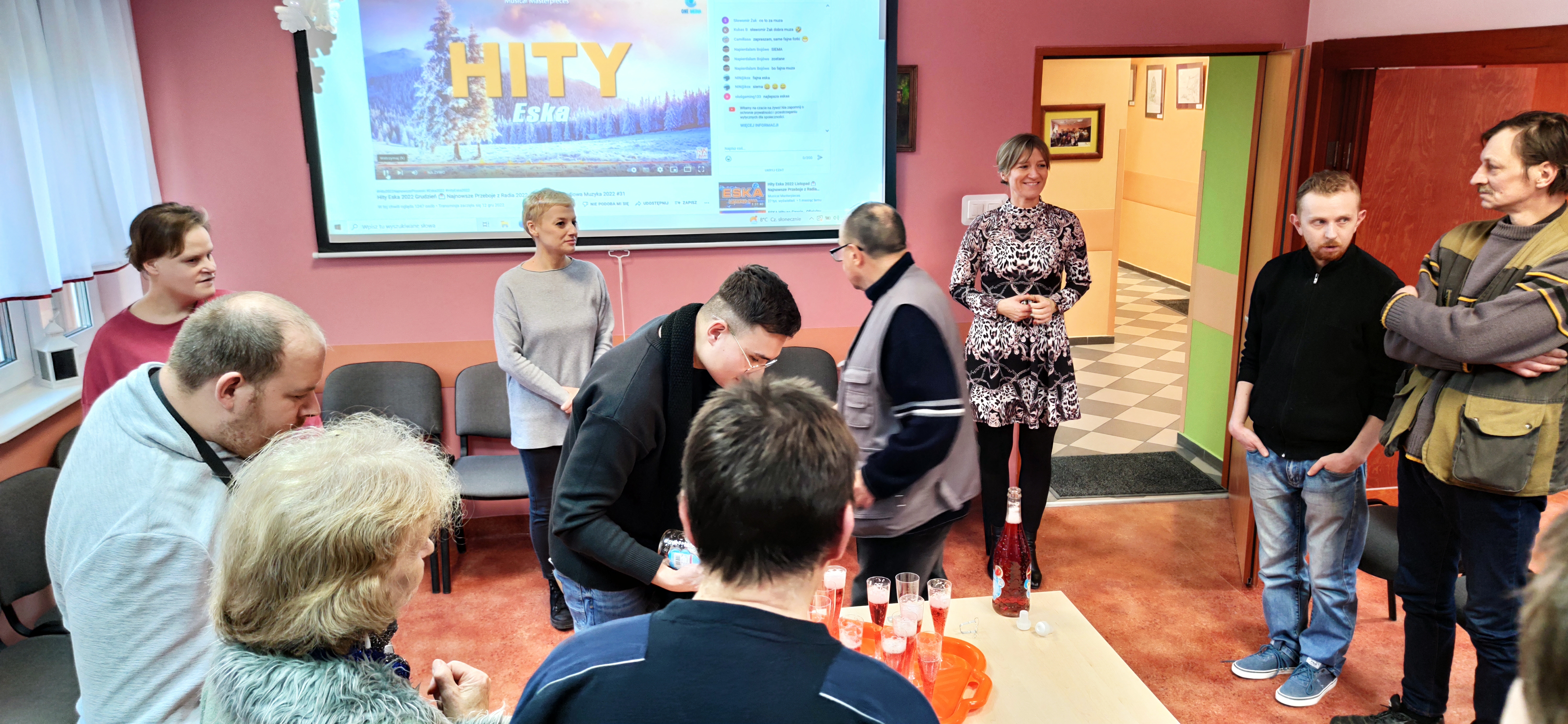 Grupa osób sto i czeka na kieliszek szampana,który nalewa mężczyzna.