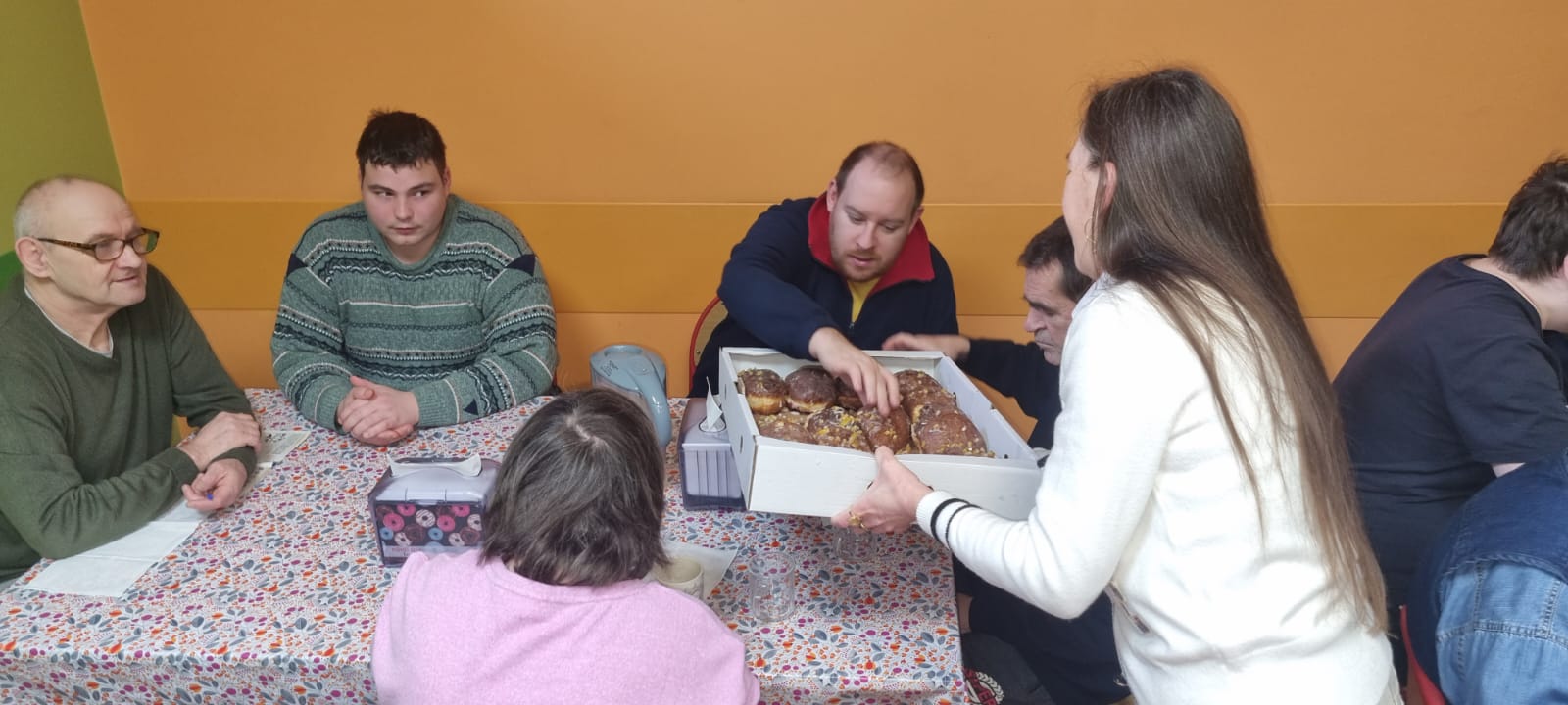 Kobieta rozdaje z kartonika pączki na stołówce uczestnikom.
